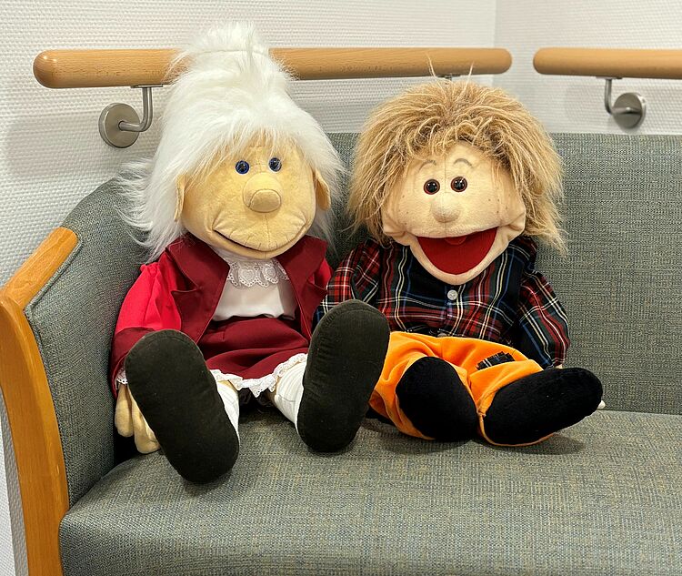 Tagespflege Henry "Am Markt" - Henry und Henriette Zwei Handpuppen mit den Namen Henry und Henriette sitzen auf einer Bank im Flur der DRK-Tagespflege Henry "Am Markt"