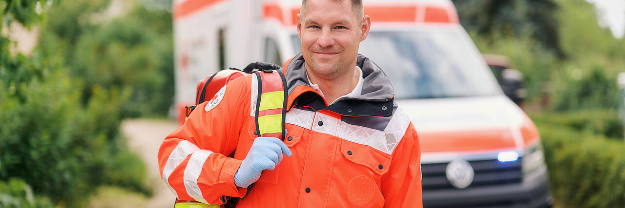 Ein Mann mit Notfallausrüstung und Rettungsjacke steht vor einem Rettungswagen