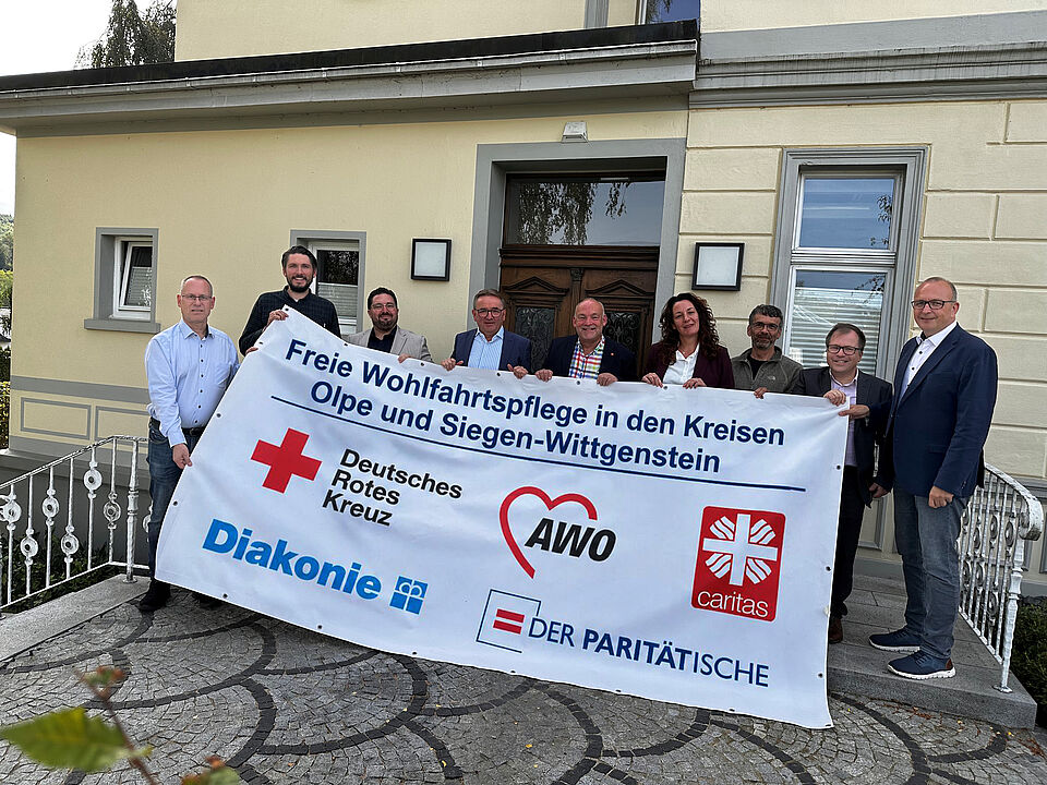 Vertreterinnen und Vertreter der Arbeitsgemeinschaft der Freien Wohlfahrtspflege aus den Kreisen Olpe und Siegen-Wittgenstein stehen hinter einem Banner
