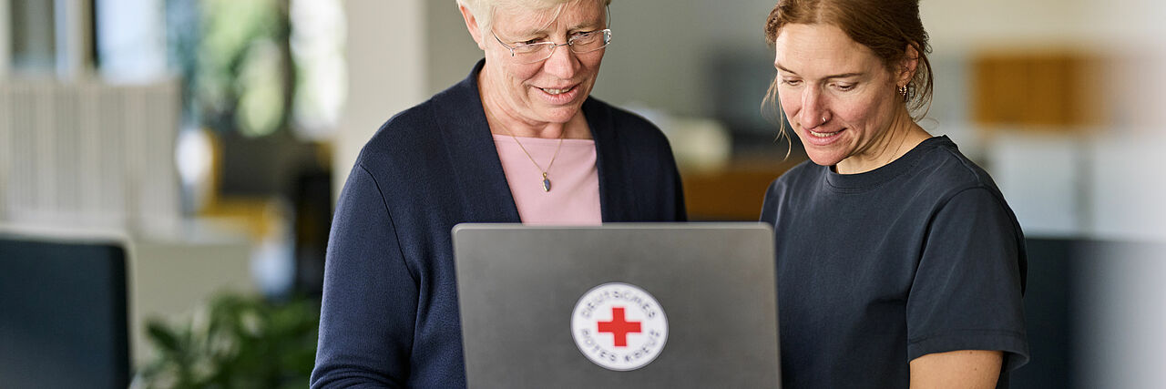 Zwei Frauen unterschiedlicher Generationen schauen gemeinsam auf einen Laptop mit den Angeboten des DRKs
